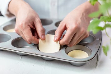 Ausgestochene Blätterteigkreise werden in die Mulden eines Muffinblechs gelegt.