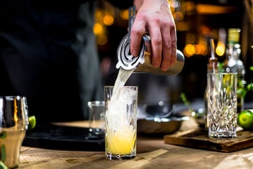 Drink mit dem Barsieb in ein Longdrinkglas abseihen
