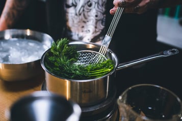 Dill wird mit einer Schaumkelle in einen Topf mit heißem Wasser gegeben.
