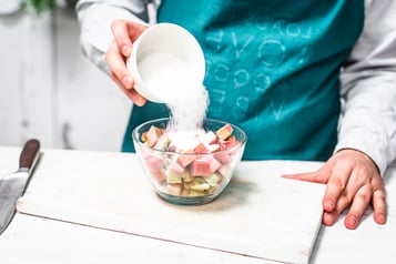 Zucker wird zu dem geschnittenen Rhabarber in eine Glasschüssel gegeben.