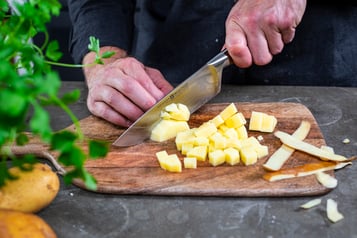 Kartoffel wird auf Holzbrett mit Messer gewürfelt