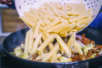 Penne werden in Artischocken mit Weißwein in Bratpfanne gegeben