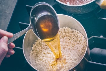 brühe wird mit Kelle zum Risottoreis gegeben