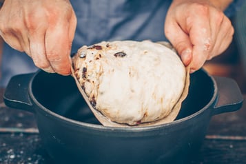 Teig für No Knead Bread wird mit 2 Händen in einen Topf gegeben