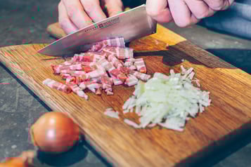 Speck und zwiebeln werden für Rösti trentino auf Holzbrett geschnitten