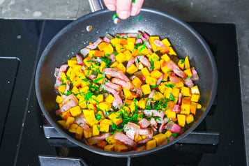 Guanciale und Kürbiswürfel in Pfanne mit Petersilie