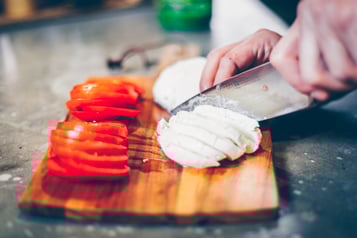 Strauchtomaten und Büffelmozzarella werden auf einem Holzbrett in Scheiben geschnitten.