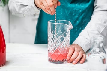 Der pinke Drink wird mit einem Barlöffel in einem hohen Glas umgerührt.