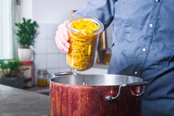 Glasgefäß mit Penne, die in Kupfertopf gegeben werden
