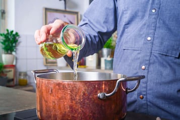 Koch gießt Weißwein aus Glasgefäß in Kupfertopf