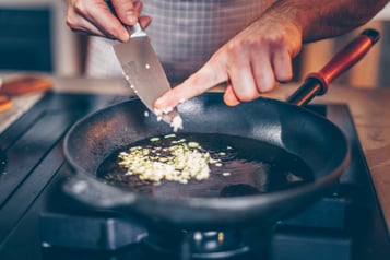 Gehackter Knoblauch wird in eine Pfanne mit heißem Öl gegeben
