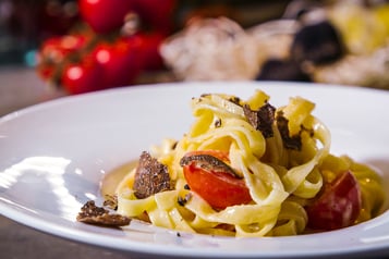 Tagliatelle mit Trüffeln und Kirschtomaten in Nahaufnahme auf weißem Teller