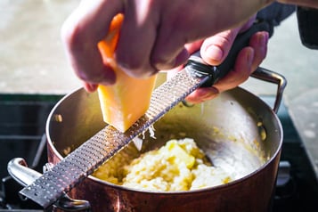 Parmesan mit Reibe in den Risottotopf hobeln