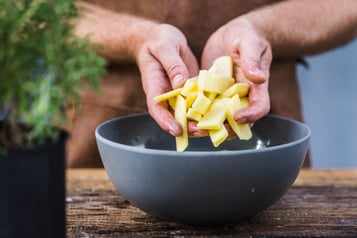 Hände legen Kartoffelsticks in eine Schale mit kaltem Wasser