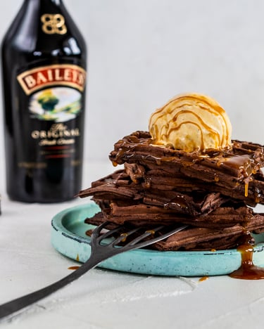Türkiser Teller mit mehreren Schoko-Waffeln übereinander gestapelt und mit einer Kugel Vanilleis und Baileys-Sauce getoppt.