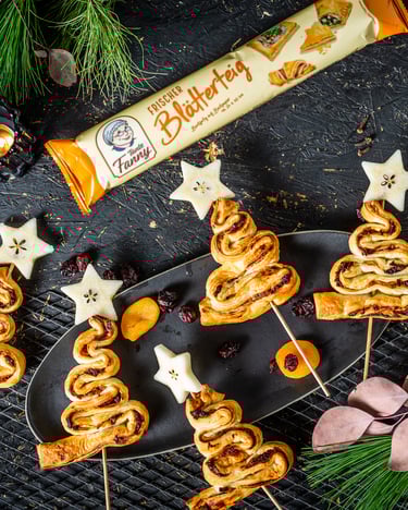 Weihnachtsbäume aus Blätterteig am Stiel auf einem Teller neben weihnachtlicher Deko und einem Glas Glühwein von oben