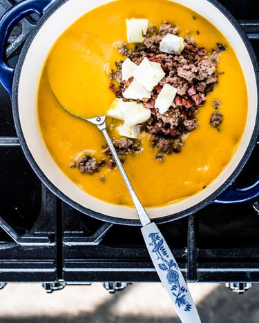 Kürbissuppe mit Speck, Hack und Käse im Topf auf einem Gasherd.