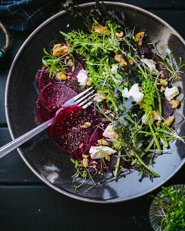 Rote-Bete-Carpaccio mit Ziegenkäse und Portulak auf schwarzem Teller und dunklem Holz