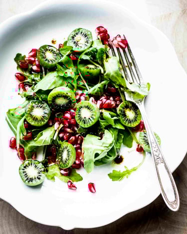 Auf einem weißen Teller liegt Kiwibeeren-Salat mit Granatapfelkernen