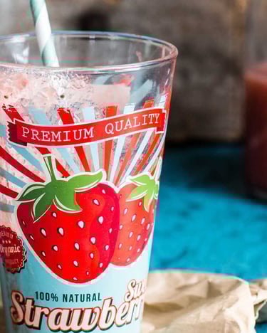 Buntes Glas mit Erdbeer-Druck neben Flasche mit Erdbeer-Smoothie auf blauem Untergrund