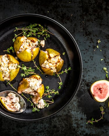 Gegrillte Feigen mit Schafskäsefüllung, kreuzförmig eingeschnitten und von oben fotografiert, etwas Thymian liegt auch auf dem Teller.