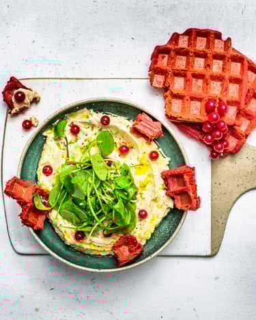 Rote-Bete-Buchweizen-Waffel neben einem Teller mit Hummus und Johannisbeeren und Portulak.