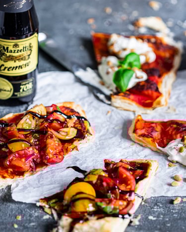 Blätterteig-Pizzette mit Tomaten und Ricotta, daneben eine Flasche Mazzetti Cremoso