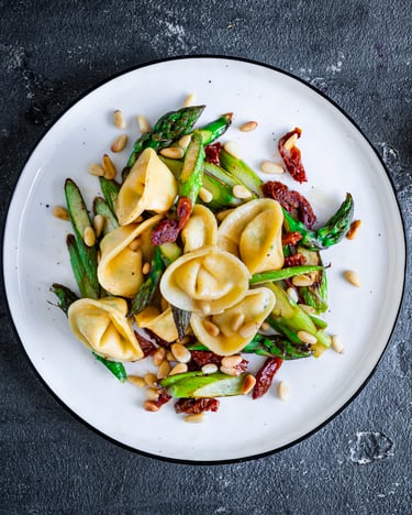 Tortellini mit Taleggio und grünem Spargel auf weißem Teller mit Besteck auf dunklem Hintergrund