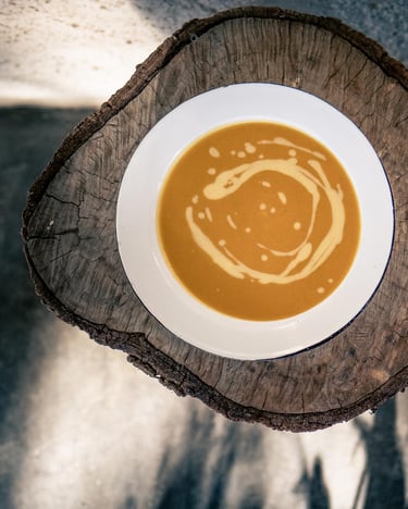 Kürbissuppe in weißem Teller auf einer Holzscheibe von oben fotografiert.