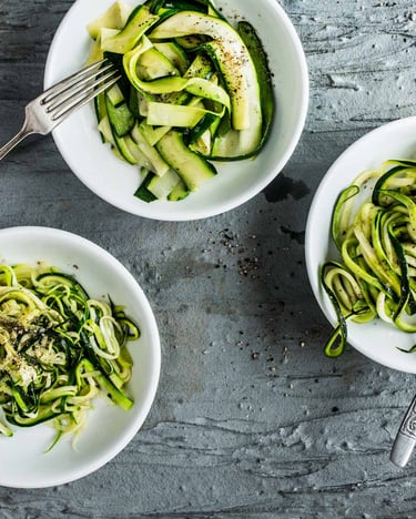 Drei Schälchen mit Zucchini-Nudeln, alle mit unterschiedlicher Form auf grauem Untergrund.
