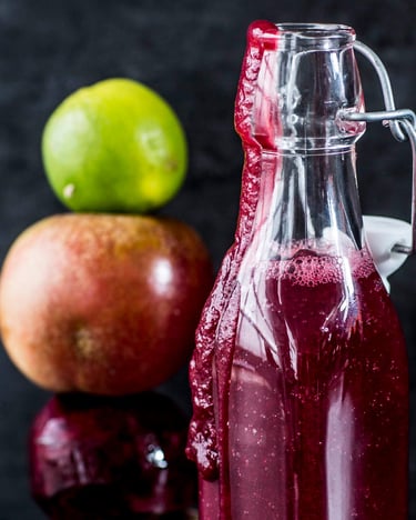 Glasflasche mit rotem Smoothie neben gestapeltem Turm aus ganzer Rote-Bete-Knolle, Apfel und Limette