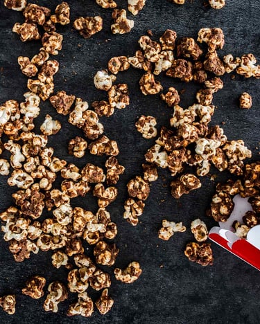 Popcorn mit Erdnussbutter und Karamell in gestreiften Popcorntüten auf dunklem Untergrund