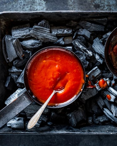 Rote BBQ-Sauce in gusseisernen Schalen auf schwarzer Kohle.