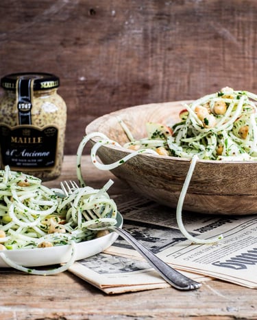 Kohlrabi-Apfel-Salat in einer Salatschüssel aus Holz und auf Tellern serviert neben einem Senfglas.