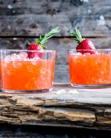 Zwei Erdbeer-Daiquiri im Glas auf einem Holzstrück neben einem Korb voll frischer Erdbeeren