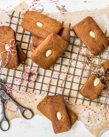 Eckige Lebkuchen mit Mandeln auf Backpapier und einem Gitter.