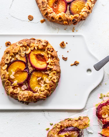 Runde Galettes mit Pflaumen-Hälften auf weißem Keramik-Tablett.