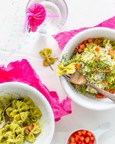 Farfalle mit Pesto-Sahnesauce in zwei Schüsseln auf weißem Untergrund mit pinken Servietten