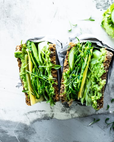 Vollkorn Sandwich großzügig belegt mit Avocadocreme, Salat, Gurke und Kresse auf grauer Marmorplatte