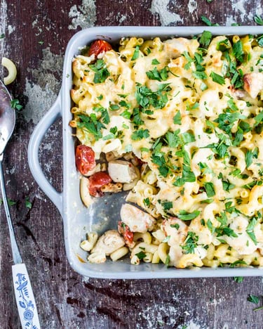 Nudelauflauf mit Hähnchen und Kirschtomaten in einer Auflaufform, fotografiert von oben auf hölzernem Untergrund.