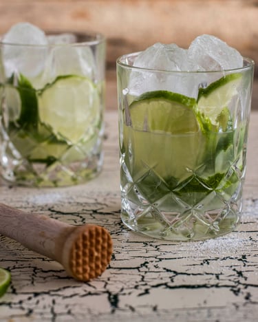 zwei Caipirinha im Glas mit Eiswürfeln und einem Stößel