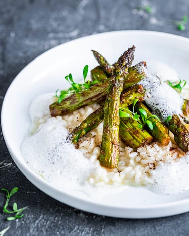 Risotto mit grünem Spargel und Pfefferschaum auf weißem Teller mit hohem Rand auf dunklem Untergrund