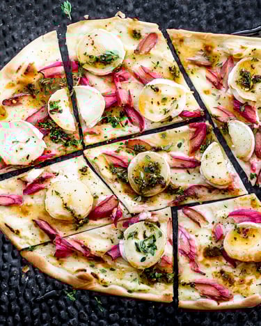 Flammkuchen mit Ziegenkäsetalern, Rhabarber und Kräutern auf schwarzem Backblech.