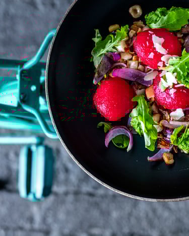 Schwarze Schale mit Rote Bete-Knödeln und Salat auf dem Gepäckträger von einem türkisem Fahrrad.