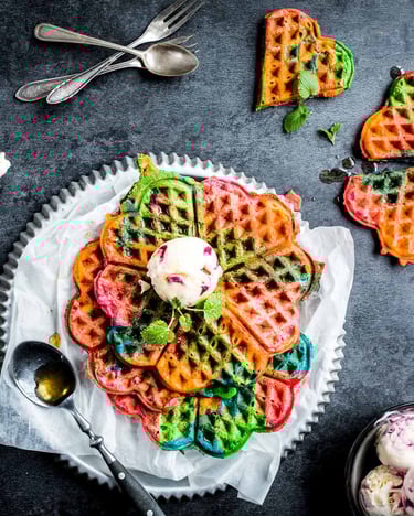Selbst gemachte Regenbogen-Waffeln mit Eis auf einer Servierplatte und dunklem Untergrund