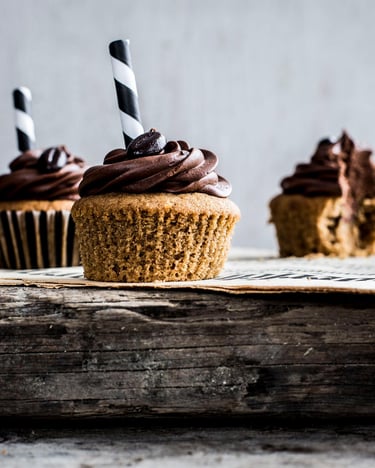 Cupcakes mit flüssigem Kaffeekern und einer schokoladigbraunen Cremehaube mit Kaffeebohnen auf einem dicken Holzbrett
