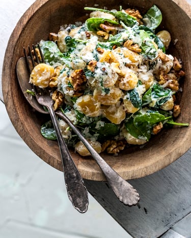 Holzschale gefüllt mit Gnocchi, Ricotta, Spinat, Walnüssen und Parmesan Topping auf weißem Tisch.