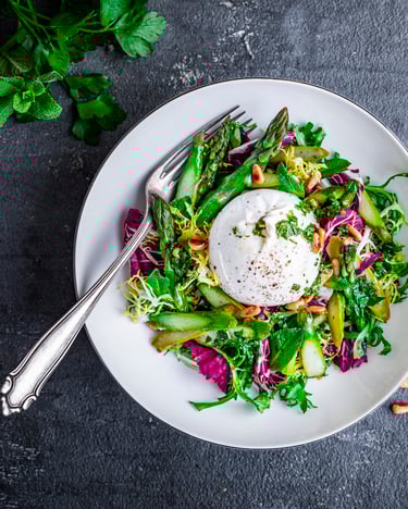 Salat mit Spargel und Burrata auf weißem Teller mit Gabel vor dunklem Hintergrund