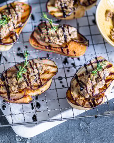 5 Scheiben Bruschetta mit Auberginenmus und gegrillter Aubergine, mit Balsamicocreme verziert, daneben eine Flasche Mazzetti Cremaceto Classico