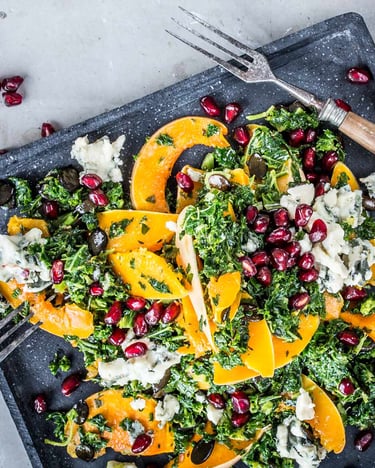 Bunter Salat mit Grünkohl, Kürbis und Granatapfel auf eckigem dunklen Teller